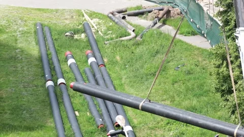 Long, black, pre-insulated pipe with red end caps being lifted by crane strap Stock Footage 344864209
