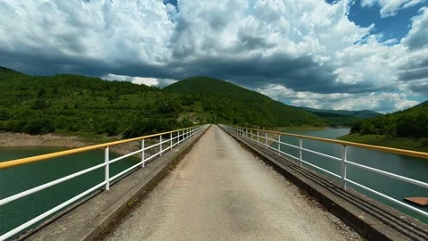 Long bridge spans calm waters between lush green hills. Zavoj Lake, Serbia Stock Footage 337488172