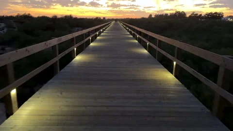 Long bridge walkway illuminated by soft lights leads into a colorful sunset hori Stock Footage 291314352