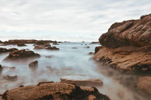Long camera exposure of ocean waves against rocky shore Stock Photos
