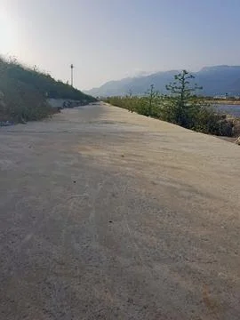 Long cement path half in shade &amp; half in sunlight, stretches out against distant Stock Photos