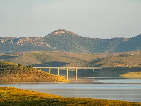 Long Concrete Bridge Crossing a Scenic Reservoir Beneath Rugged Mountain Peaks Stock Photos