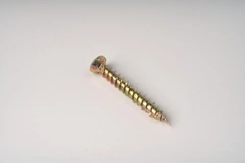 A long construction self-tapping screw of golden color on a white background. Stock Photos