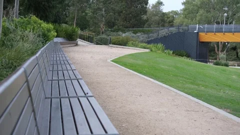 A long contemporary public park bench stretches along a pathway Vídeos de archivo 336034588