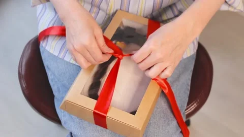 Long cut braid in gift box with red ribbon in hands, haircut donation, unboxing Video stock 194493836