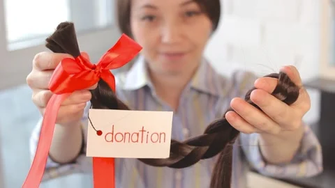 Long cut braid with tag and red ribbon bow in woman hands, donation of haircut Video stock 194121040