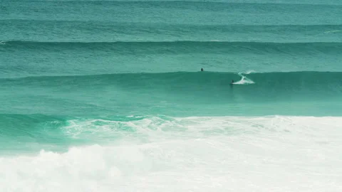 Long distance view of pro surfer riding on ocean waves near jet ski driver Stock Footage 163265058