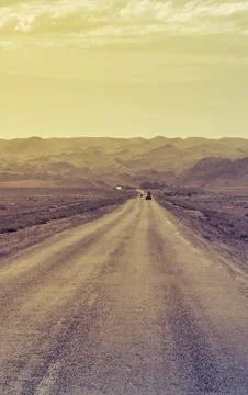 Long empty asphalt road stretching through arid landscape towards distant m.. Фото
