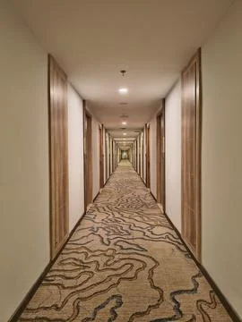 Long empty hotel corridor with patterned carpet and wooden doors Stock Photos