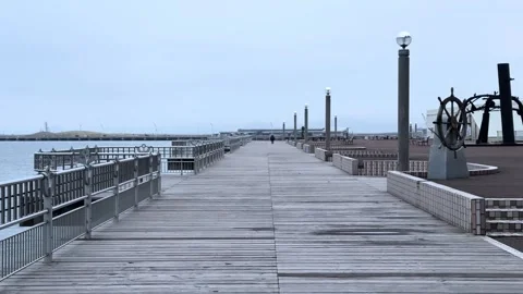 Long empty pier on Aomori Bay with shipwheel sculpture and calm overcast Stock Footage 309524662