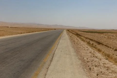 A long, empty road extends through the dry terrain of Kunduz Province, showca Stock Photos