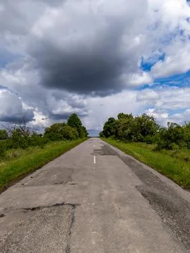 A long empty road in the middle of a grassy field under a cloudy sky Stock-Fotos