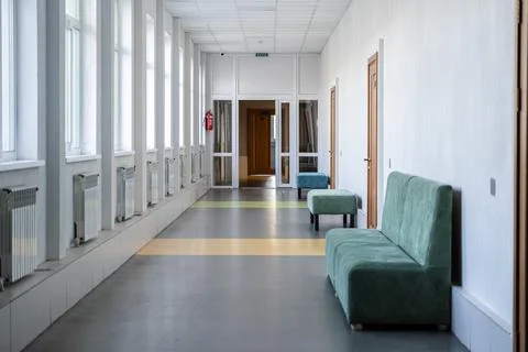 Long empty school corridor with green velvet benches and large bright windo.. Stock Photos