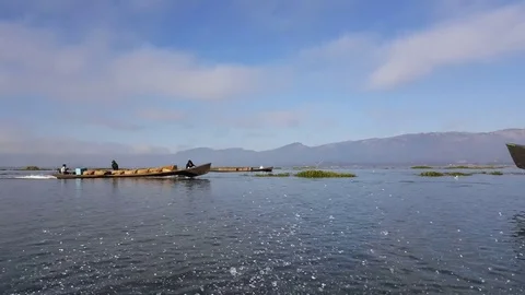 Long engine boat enters shot, man sits in boat, boatman, mountains, Inle Lake Vídeos de archivo 79790592