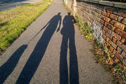 Long evening shadows of a man and woman walking the dog on a leash Stock Photos