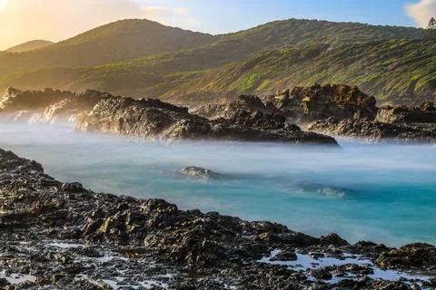 A long exposure captures waves softly washing over a rugged rocky coastline Stock Photos