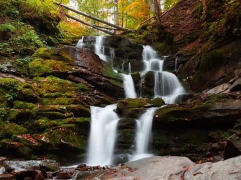 Long exposure of high waterfall is flowing on the rock in autumn forest Stock Photos