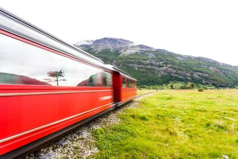 Long exposure of red train riding along green grassy field Stock Photos