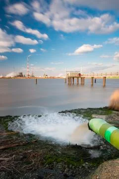 Long exposure shot of a wastewater pipe and a large oil refinery in the harbo Stock Photos