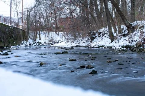 A Long Exposure of a Small Creek Next to a Snow Covered Bank Stock Photos