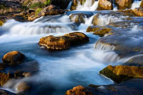 Long exposure of a small stream gently flowing over rounded rocks Stock Photos