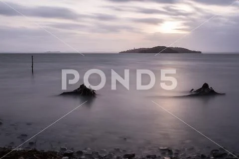 Long exposure view of Trasimeno lake (Umbria) shore, with branches, stones and Stock Photos