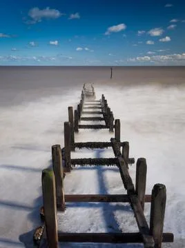 Long exposure of waves rolling over wooden groyne, Overstrand Beach, Norfolk, UK Foto stock