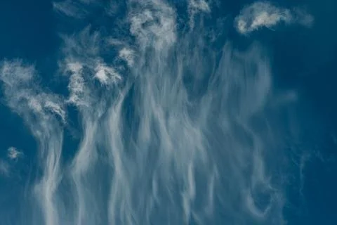 Long, feather-like wisps of white clouds stretch across a rich blue sky. Stock Photos