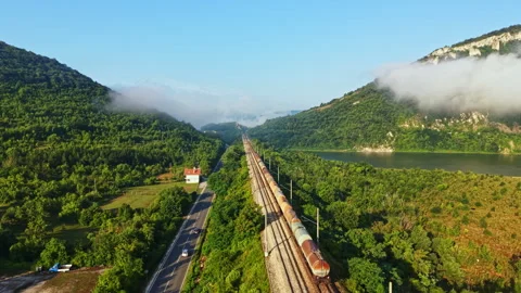 Long freight train moving through green valley between forested hills under Stock Footage 340958174