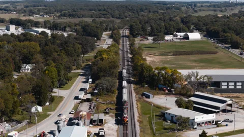 Long freight train passing businesses and open land in Gentry, Arkansas Stock Footage 345342874