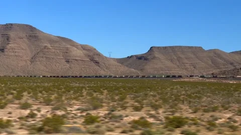 Long freight train speeds through vast desert landscape with rugged mountains on Stock Footage 304734321