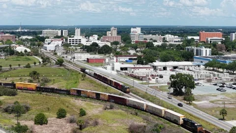 Long freight train winds past Bonnet Springs toward downtown Lakeland skyline Stock Footage 339994352