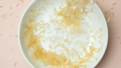Long grain parboiled uncooked basmati rice pours into a plate close-up. 스톡 동영상 268440288