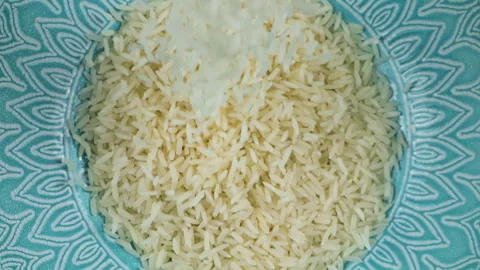 Long grain rice is poured into a ceramic blue bowl. Top view. Slow motion.	 库存影片 304392827