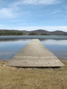 Long gray dock points into a half-frozen mountain lake in spring time in mont Stock Photos