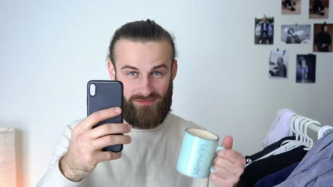 Long hair guy  is looking in a mirror doing selfie &amp; and drinking coffee Stock Footage 147897909