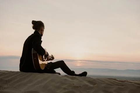 Long haired bearded guy with guitar sitting in the sunset Stock Photos