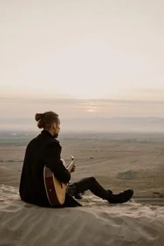 Long haired bearded guy with guitar sitting in the sunset Stock Photos