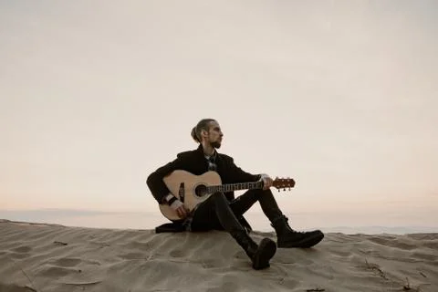 Long haired bearded guy with guitar sitting in the sunset Stock Photos