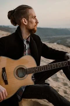 Long haired bearded guy with guitar sitting in the sunset Stock Photos