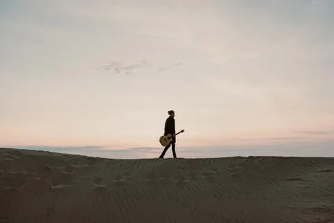 Long haired bearded guy with guitar standing in the sunset Stock Photos