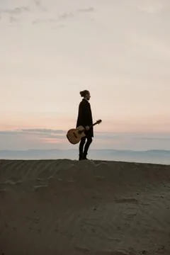 Long haired bearded guy with guitar standing in the sunset Stock Photos
