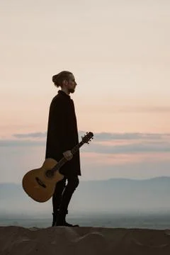 Long haired bearded guy with guitar standing in the sunset Stock Photos