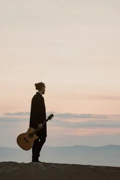 Long haired bearded guy with guitar standing in the sunset Stock Photos
