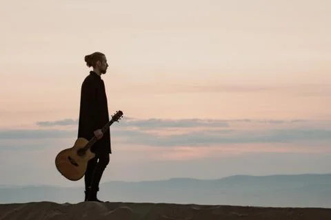 Long haired bearded guy with guitar standing in the sunset Stock Photos