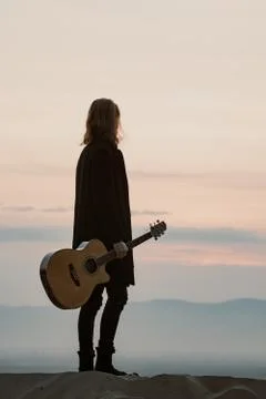 Long haired bearded guy with guitar standing in the sunset Foto stock