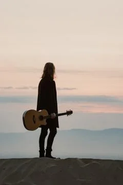 Long haired bearded guy with guitar standing in the sunset Stock Photos