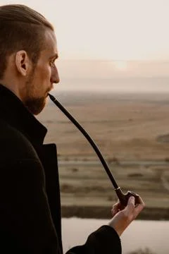 Long haired bearded guy smoking pipe in the sunset Stock Photos
