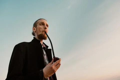 Long haired bearded guy smoking pipe in the sunset Stock Photos