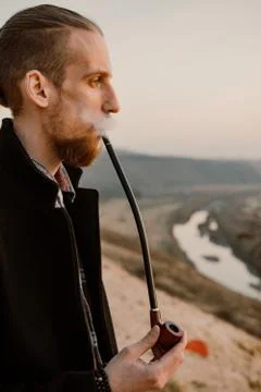 Long haired bearded guy smoking pipe in the sunset Stock Photos